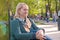 Portrait in profile of middle-aged woman sits on the bench of pond in city park