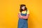 Portrait of puzzled disconcerted girl teenager in french beret, denim sundress holding hands crossed isolated on yellow