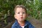 Portrait of a puzzled toddler boy against of green foliage background