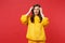 Portrait of puzzled upset disgusted young woman in yellow fur sweater putting hands on head isolated on bright red