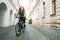 The portrait of Red curled long hair caucasian teen girl on the cobblestone city street riding a bicycle. Natural people beauty