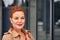 Portrait of a red-haired middle-aged woman in a brown cloak  while walking around the city. Cloudy summer evening.