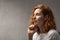 Portrait of red-haired woman on gray background side view. Pensive beautiful girl