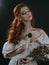 Portrait of a red-haired young woman in a vintage gold dress with a dry bouquet in hands on a black background. A princess. Fairy