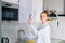 Portrait of redhead young woman opening door of kitchen cabinet at light kitchen room.