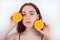 Portrait of redheaded young woman looking natural standing on isolated white background holding halves of orange in her hands near