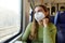 Portrait of relaxed female commuter wearing medical protective mask looking through the window sitting on train