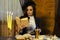 Portrait of Relaxing Brunette Woman Posing in Retro Style Dress With Coffeepot and Jam While Reading Book At The Table Indoors