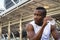 Portrait of relaxing young african american sportsman sitting and drinking water from bottle after running exercise in city in