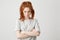 Portrait of resentful young pretty redhead girl looking at camera brutally with crossed arms over white background.