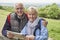 Portrait Of Retired Couple On Walking Holiday Resting On Gate With Map