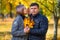 Portrait of romantic couple in autumn city park, woman whispers bad news to man, and he is very unhappy, yellow leaves and bright