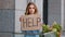 Portrait sad fired poor caucasian millennial business woman standing in city looking at camera holding cardboard sign