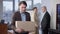 Portrait of sad fired young man standing in office with box as blurred colleagues talking at background. Stressed upset