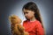 Portrait of sad or unhappy girl playing with teddy bear isolated on gray