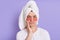 Portrait of sad upset young man in towel use eye anti-wrinkle patches posing isolated over purple background, expressing sorrow,