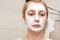 A portrait of a sad woman with problem acne skin making a cleansing purifying white facial mask, anti black spot and acne