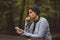 Portrait of sad woman sitting alone in the forest with smartphone. Solitude concept. Millenial dealing with problems and