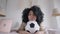 Portrait of sad young woman lying on bed with soccer ball looking at camera. Upset beautiful African American lady