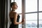 Portrait of a sad young woman with short hair standing looking out the window in a black dress