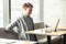 Portrait of sadness painful tired bearded young freelancer in grey blazer are sitting alone in cafe and holding his back with