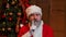 Portrait of Santa Claus looking pensively around, makes secret gesture and winks. Old man in red suit and hat against