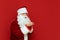 Portrait of Santa standing on red background looks at raised hands and sends an air kiss, looks away. Christmas concept. Happy