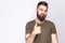 Portrait of satisfied bearded man with thumbs up and dark green t shirt against light gray background.