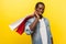 Portrait of satisfied buyer, positive man holding shopping bags on his shoulder. indoor studio shot isolated on yellow background