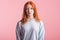 Portrait of a satisfied redhead girl in the studio on a pink background.