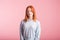 Portrait of a satisfied redhead girl in the studio on a pink background.