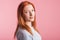 Portrait of a satisfied redhead girl in the studio on a pink background.