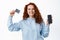 Portrait of satisfied redhead woman with curly hair, smiling pleased, showing empty smartphone screen and plastic credit