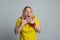 Portrait of scared mature woman with hands near face, wearing casual yellow t shirt. Studio shot, gray background