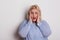 Portrait of a scared overweight woman in studio, hands on cheeks.