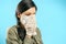 Portrait of a scared woman in a surgical mask covering her face with hands in protective gloves on a blue background