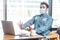 Portrait of scared young businessman with surgical medical mask in blue shirt sitting, shocked looking at laptop display with