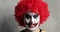 Portrait of scary angry man clown with Halloween makeup and red curly wig.