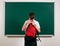 Portrait of a school boy looking for school supplies in his backpack, blackboard background - back to school and education concept