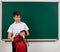 Portrait of a school boy looking for school supplies in his backpack, blackboard background - back to school and education concept