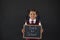 Portrait of schoolgirl holding slate with text against blackboard