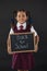 Portrait of schoolgirl holding slate with text against blackboard