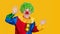 Portrait of a screaming clown with copyspace on yellow background. Funny kid in green wig in clown costume.