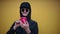 Portrait of self-confident cheerful hipster, wearing all black, using smartphone with pink case, on background of yellow wall.