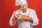 A portrait of a senior baker holding croissant isolated on red background