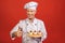 A portrait of a senior baker holding delicious cakes isolated on red background. Thumbs up