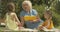 Portrait of senior Caucasian woman in eyeglasses reading book for cute little girls outdoors. Happy grandmother spending