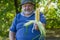 Portrait of senior farmer giving ripe ear of maize while sitting under tree shadow