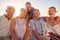 Portrait Of Senior Friends Sitting On Rocks By Sea On Summer Group Vacation