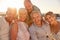 Portrait Of Senior Friends Sitting On Rocks By Sea On Summer Group Vacation